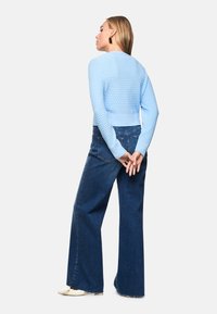 Light blue textured cropped sweater with a round neckline paired with dark blue wide-leg jeans. Model stands with hands behind back.