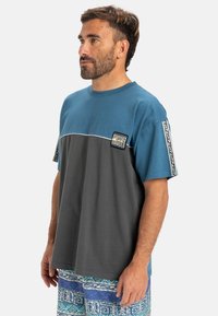 Korte mouw shirt: blauwe bovenkant, grijze onderkant, witte naden, logo op de voorkant, tekstuele mouwaccenten, relaxte pasvorm.