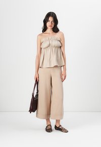 Haut beige sans bretelles avec une texture froncée ; large pantalon beige clair ; ballerines à motifs léopard noir et tan ; sac à main marron avec anse.