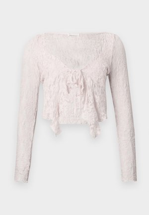 Svetlo rožnata kratka majica iz čipke z dolgimi rokavi, V-izrezom in vezalko spredaj. Celotno površino krasi teksturiran cvetlični vzorec.