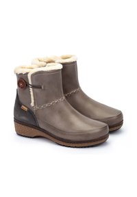 Bottes chelsea en cuir marron avec doublure en fausse fourrure, couture décorative et semelle intermédiaire en liège. Présente un bouton rond sur le côté.