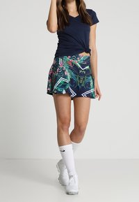 T-shirt navy a V con dettaglio annodato abbinato a una gonna corto con motivo tropicale caratterizzata da colori vivaci e accenti geometrici bianchi.