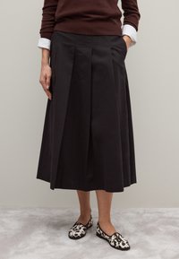 Gonna nera plissettata con tasche laterali, realizzata in tessuto, abbinata a scarpe slip-on con motivo che presentano accenti in bianco e nero.