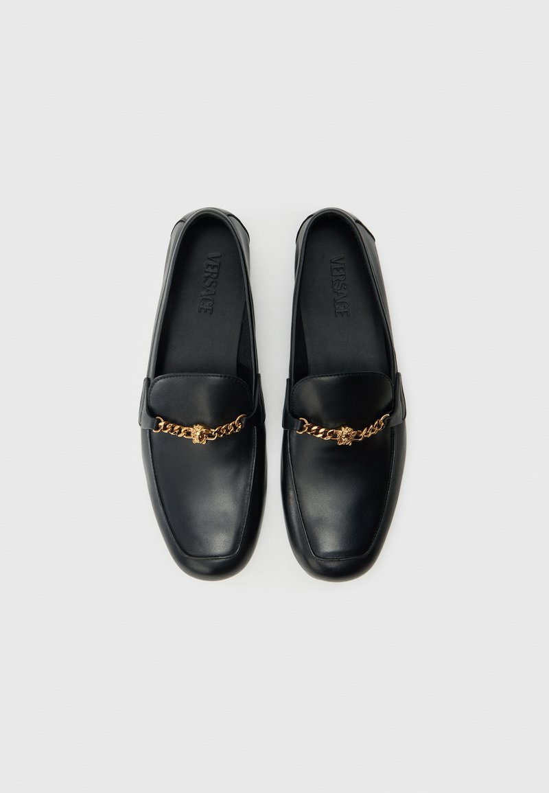 Sorte læderloafers med en guldkæde og et logo på indersålen. Designet er elegant med en firkantet tå og glat tekstur.