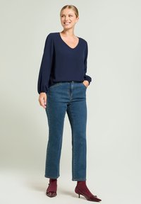 Granatowa bluzka z dekoltem w kształcie litery V, z balonowymi rękawami; w połączeniu z niebieskimi dżinsami. Modelka nosi bordowe skarpetki i buty na spiczastym nosku.