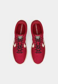 Red canvas sneakers with black laces, white star accents, and a cream rubber sole. Features a round toe and cushioned interior.