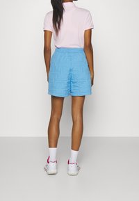 Blue quilted shorts with an elastic waistband, paired with a pink polo shirt and white shoes with pink accents.