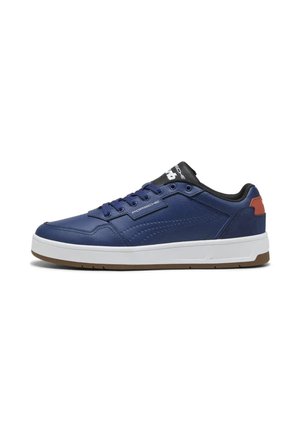 Sneaker basso blu navy con suola bianca, battistrada marrone scuro, collarino imbottito nero e logo Porsche sul lato e sulla linguetta.