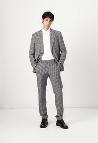 Grå och svart houndstooth kostym med skräddarsydd passform, bärs över en vit skjorta; har eleganta svarta kostymskor och en ren, minimalistisk bakgrund.