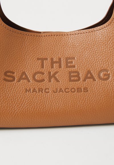 Kohvashall nahk õlakott, millel on reljeefne tekst: "THE SACK BAG MARC JACOBS." Pinna viimistlus on tekstuuriga ja servi on sujuvad.