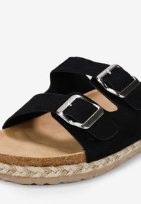 Sandale en suede noir avec deux straps ajustables ornés de boucles argentées, une semelle intérieure en liège naturel et une semelle en jute tressé.