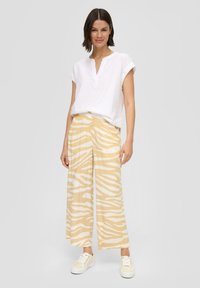 Witte short-sleeve button-up top gecombineerd met gele brede broek met een witte zebra-streep patroon. Model draagt lichte sneakers.