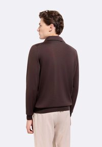 Polo marrone a maniche lunghe con colletto, realizzato in tessuto liscio. Presenta un design aderente e polsini a costine. Stile minimalista.