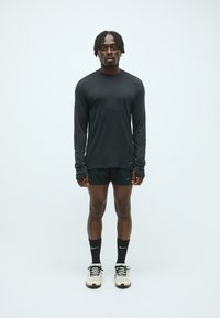 Crna dugosleeve atletska majica, crne kratke hlače, crne čarape i svijetli tenisice. Teksturedna tkanina s Nike logotipom na majici i obući.