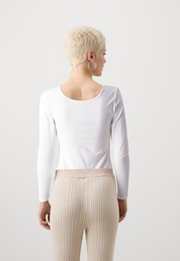 Hvit langermet topp med scoop-back, kombinert med beige ribbede høyt midje bukser. Glatt stoff og tettsittende design understreker enkelhet.