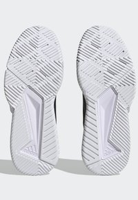 White athletic shoe soles with textured rubber for grip, showing a zigzag pattern and a logo, designed for traction and durability.