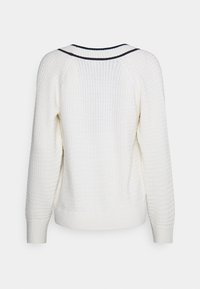 Hvid strikket sweater med et tekstureret mønster, raglanærmer og en kontrasterende mørkstribet halsudskæring; ribbet manchetter og kant.