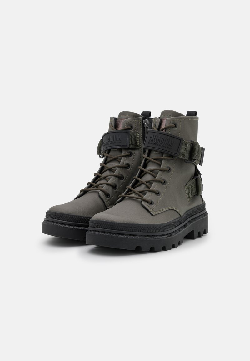 Botas de tobillo verde oliva con suela negra resistente, cierre de cordones en la parte delantera y cremallera lateral. Presentan una correa con logo en el tobillo para mayor soporte.