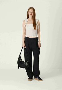 Top curto branco texturizado com alças atadas; calças pretas largas; bolsa preta; ténis pretos com solas claras; design suave e minimalista.