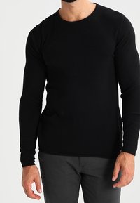 Zwarte top met lange mouwen, gemaakt van een soepel, rekbaar stof met een ronde halslijn en subtiele geborduurde details op de borst.