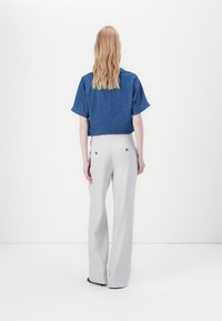 Blauwe denim cropped blouse met korte mouwen, gecombineerd met hooggetailleerde, lichtgrijze flared broeken met achterzakken en gouden accenten.