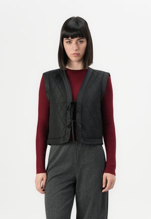 Black quilted vest with a tie closure, featuring a sleek design. Worn over a textured burgundy sweater and gray patterned trousers.