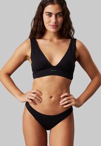 Conjunto de bikini negro que incluye un bralette triangular y parte inferior de cintura baja. Está hecho de una tela suave con un diseño minimalista y un pequeño detalle de logo.