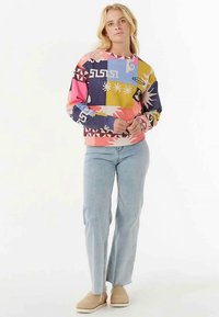 Felpa multicolore con motivi geometrici e floreali, scollo a girocollo e polsini a costine, abbinata a jeans in denim chiaro.