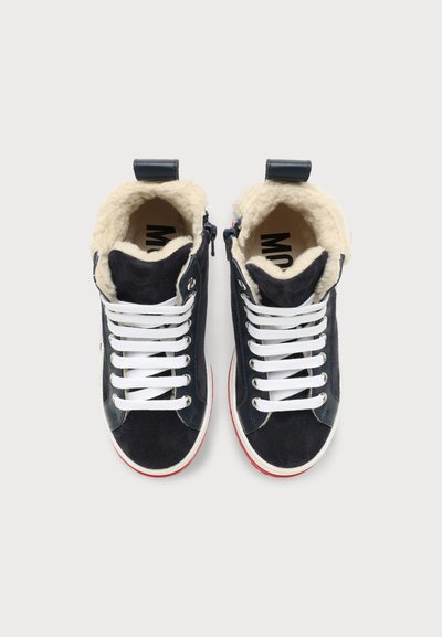 Paire de baskets montantes noires avec lacets blancs et doublure polaire beige visible au niveau des cols de cheville, vues de dessus sur fond blanc.