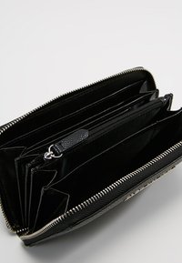 Portefeuille noir avec fermeture éclair, comportant plusieurs compartiments, y compris des emplacements pour cartes et une poche zippée, avec un intérieur lisse et texturé.
