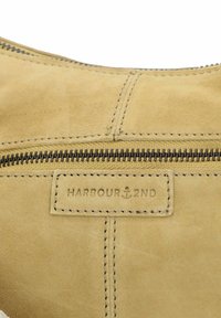 Borsa in suede marrone chiaro con una texture liscia, cuciture visibili e una cerniera metallica lungo la parte superiore. Etichetta "HARBOUR 2ND" attaccata in modo discreto.