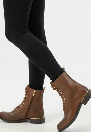 Bruine leren enkellaarsjes met gouden oogjes, ritsdetails en een chunky hak. Heeft een gladde afwerking en een gestructureerd zijpaneel.