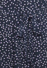 Marinblå klänning med midjeband, tillverkad av mjukt tyg med ett strukturerat mönster av lila och vita prickar.