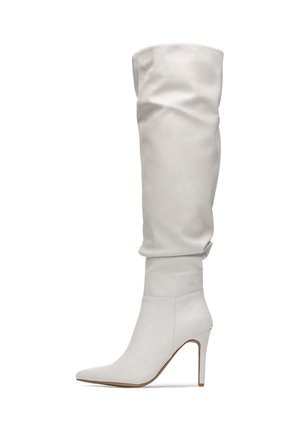Białe skórzane kozaki za kolano z fasonem luźno opadającym, spiczastym noskiem i obcasem typu szpilka. Gładka faktura i minimalistyczny styl.