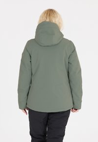 Olivgrön isolerad jacka med huva, slät textur och en något avsmalnande form. Svarta byxor är också synliga.