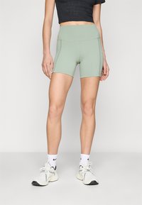 Shorts verdi a vita alta con una trama liscia e un design aderente, caratterizzati da dettagli di cucitura laterale. Indossati con scarpe da ginnastica bianche.