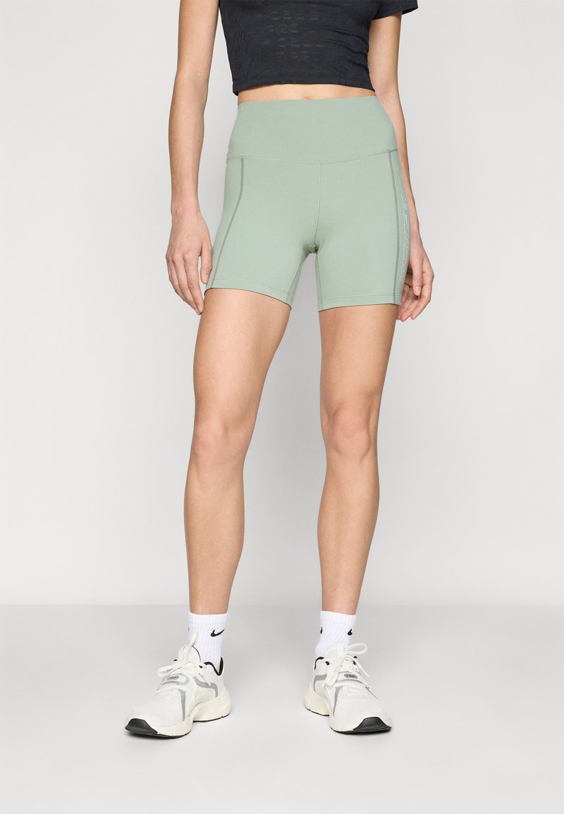 Shorts verdi a vita alta con una trama liscia e un design aderente, caratterizzati da dettagli di cucitura laterale. Indossati con scarpe da ginnastica bianche.