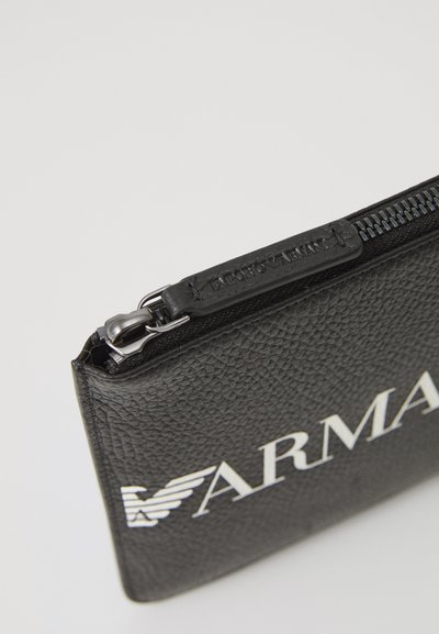 Pungă din piele texturată neagră cu fermoar argintiu, având logo-ul "ARMANI" în alb. Formă rectangulară, detaliu de branding subtil pe fermoar.