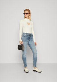 Hvid ribbet langærmet bodysuit med hjerteudskæring, lyseblå tætsiddende jeans, sort håndtaske og cremefarvede loafers med logodetalje.