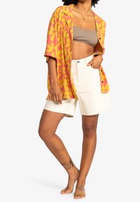 Short-sleeve shirt in pink and yellow floral pattern, paired with white denim shorts. Smooth fabric with a relaxed fit, features a button closure.