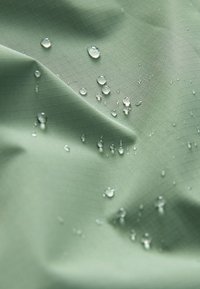 Vanddråber, der perler på en glat, lysegrøn stofoverflade med en subtil gittertekstur og bløde folder.