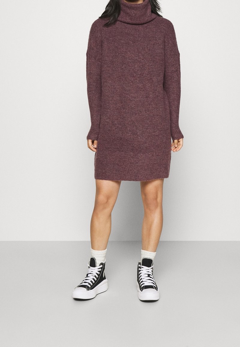 Robe à col roulé en bourgogne avec une coupe ample et des manches longues. Associée à des baskets montantes noires et des chaussettes blanches duveteuses.