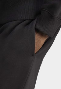 Pantaloni della tuta neri con cintura a coste e tasca laterale. Il tessuto appare liscio con una consistenza morbida, evidenziando un design a vestibilità rilassata.