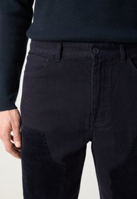Marineblauwe broek met een gladde textuur, voorzien van corduroy accenten aan de zijkanten, een vijf-pocket ontwerp en een knoopsluiting bij de taille.