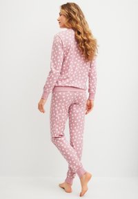 Roze pyjama set met een wit hartpatroon, bestaande uit een langemouwtop en aansluitende broek. Zachte katoen met geribbelde boorden.