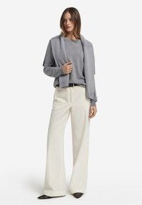 Szary sweter z dzianiny noszony na jasnoszarym topie, zestawiony z szerokimi, prążkowanymi białymi spodniami i czarnymi, szpiczastymi balerinami. Prosta sylwetka, teksturowana tkanina.