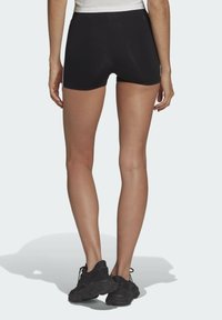 Černé sportovní šortky s hladkou texturou, středně vysokým pasem a přiléhavým střihem, v kombinaci s černými teniskami.