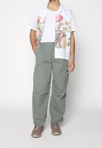 Biała koszula z krótkim rękawem w kwiatowy wzór, zestawiona z jasnooliwkowymi spodniami typu cargo. Szare trampki z akcentami w kolorze różowym. Luźny krój.