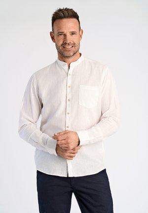 Camisa de botón de manga larga color beige claro, hecha de tejido texturizado. Presenta un cuello mandarín y un bolsillo en el pecho con botones de madera.
