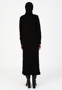 Black long-sleeve dress with a high neckline and straight silhouette. Made of soft fabric, featuring side slits at the hem and worn with black chunky boots.